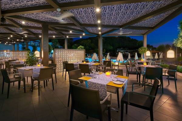 Außenbereich des Restaurants des Olympic Palace Resorts bei Nacht mit Tischen und Stühlen.
