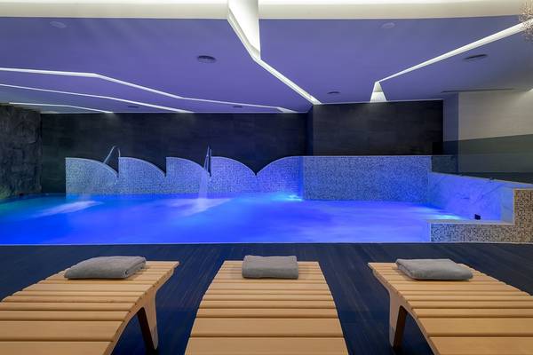 Poolbereich im Olympic Palace Resort mit blau beleuchtetem Wasser und Liegen.