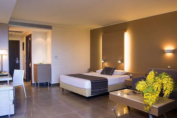 Hotelzimmer im Olympic Palace Resort mit Bett, Schreibtisch und gelben Blumen.