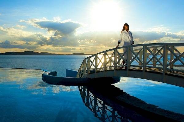 Eine Frau in einem weißen Bademantel geht über eine Brücke am Pool des Saint John Hotel Villas & Spa.