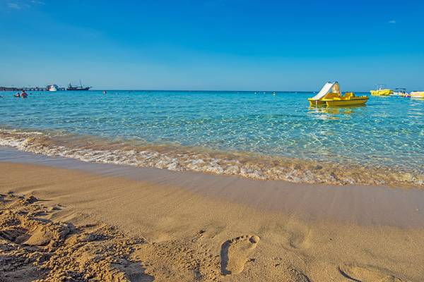 Strand des Vrissiana Beach Hotels mit gelben Booten im Wasser und braunem Sand