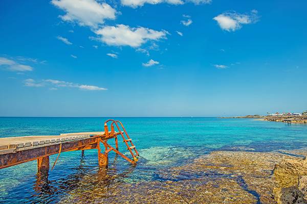 Ein Pier am Vrissiana Beach mit blauem Himmel und Ozean im Hintergrund.
