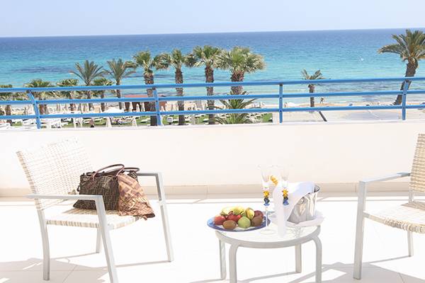 Blick vom Balkon auf das Meer im Vrissiana Beach Hotel mit Früchten auf dem Tisch und einer Tasche.