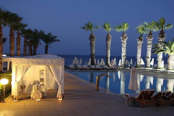 Nachtansicht des Vrissiana Beach Hotel mit Pool und Liegestühlen unter Palmen.