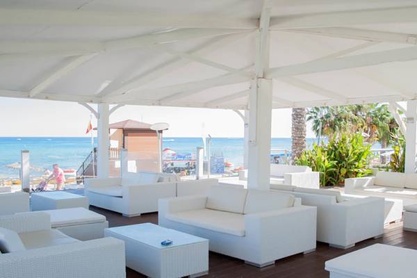 Außenbereich des Vrissiana Beach Hotels mit weißen Möbeln und Blick auf das Meer.