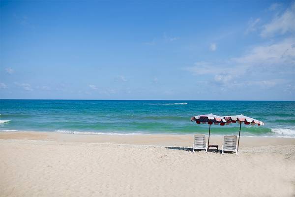 Strand mit Sonnenliegen und Sonnenschirmen vor einer ruhigen Meeresbucht