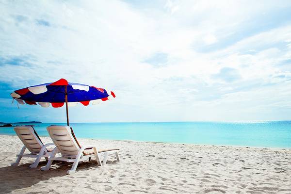 Strandszene mit zwei Sonnenliegen und einem bunten Sonnenschirm, der vor der Sonne schützt