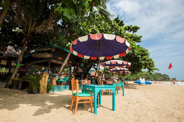 Tisch unter einem bunten Regenschirm am Strand des Fair House Beach Resorts