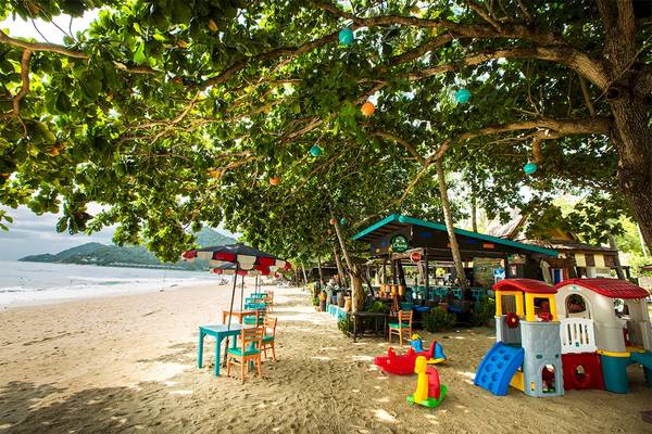 Strand mit Kinderspielplatz und Sitzbereich unter einem Baum.