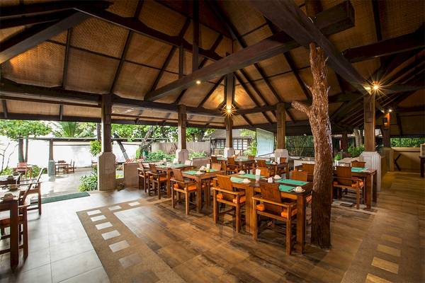 Innenbereich des Restaurants im Fair House Beach Resort mit Holztischen und Stühlen.
