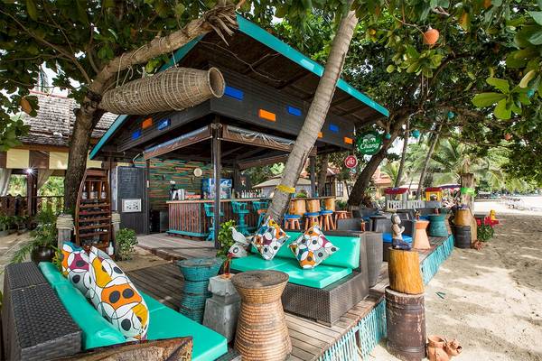 Die Bar im Fair House Beach Resort mit Strandstühlen und Sonnenschirmen.