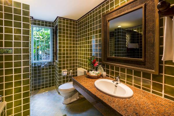 Badezimmer mit grünen Fliesen, Spiegel und Toilette neben Waschbecken.