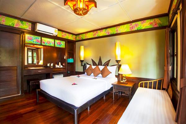 Innenansicht eines Zimmers im Fair House Beach Resort mit Doppelbett, Nachttischen und tropischer Dekoration.
