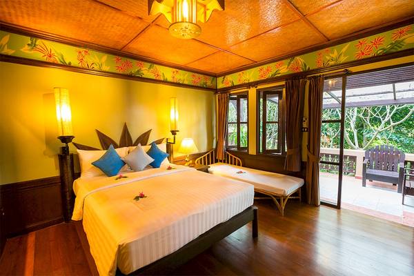 Schlafzimmer im Fair House Beach Resort mit einem großen Bett, zwei Nachttischen, einem Balkon und bunten Wanddekorationen.