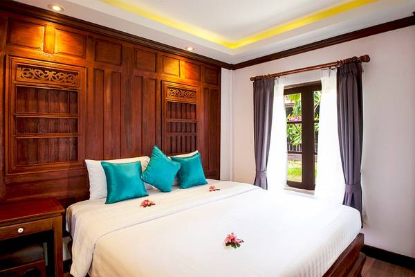 Schlafzimmer im Fair House Beach Resort mit Holzwänden, weißen Laken, blauen Kissen und Blumendekoration.