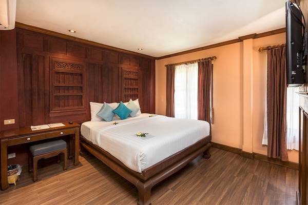 Schlafzimmer im Fair House Beach Resort mit Holzwänden, einem großen Bett und Dekoblumen.