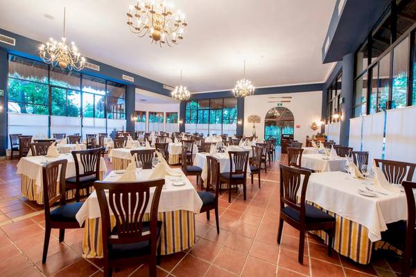 Innenansicht des Viva Wyndham Maya Hotel Restaurants mit gedeckten Tischen, Kronleuchtern und Glasfenstern.