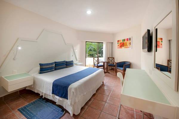 Innenansicht eines Schlafzimmers im Viva Wyndham Maya Hotel mit einem Bett, Stühlen und einem Fernseher.
