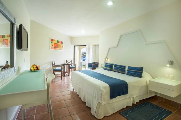 Hotelzimmer im Viva Wyndham Maya mit Bett, Tisch, Stühlen, Fernseher und Dekoration.