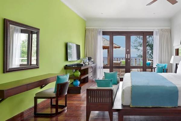 Innenansicht eines Zimmers im Hilton Seychelles Northolme Resort & Spa mit grünen Wänden, einem großen Bett und einer Aussicht auf das Meer.