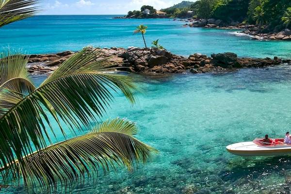 Außenansicht des Hilton Seychelles Northolme Resort & Spa mit blauem Wasser, weißen Booten und Palmen.
