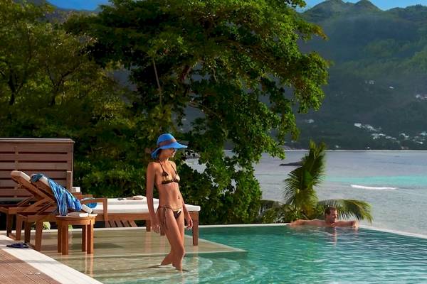 Ein Paar schwimmt im Außenpool des Hilton Seychelles Northolme Resort & Spa mit Blick auf das Meer.