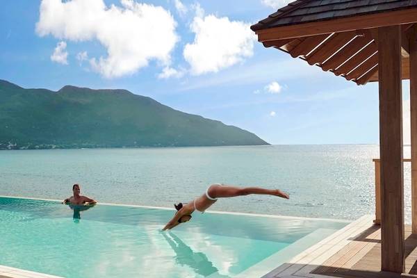 Ein Schwimmbad am Hilton Seychelles Northolme Resort & Spa mit zwei Tauchern und einer beeindruckenden Bergkulisse.