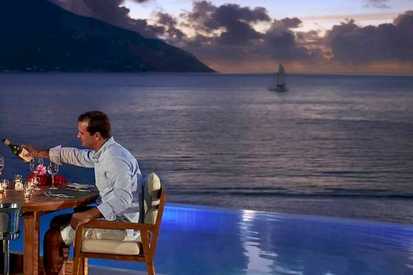 Paar sitzt am Tisch neben dem Pool und genießt ein Abendessen mit Blick auf das Meer und eine Segelyacht.