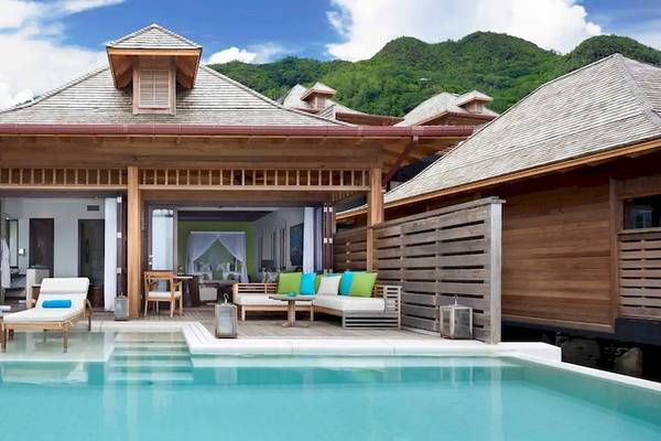Außenbereich des Hilton Seychelles Northolme Resort & Spa mit Swimmingpool, Lounge-Sesseln und Blick auf Berge.