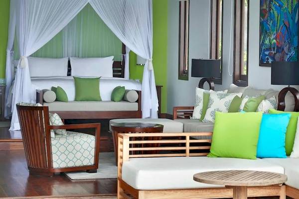 Innenansicht eines Zimmers im Hilton Seychelles Northolme Resort & Spa mit grünen und blauen Kissen auf dem Sofa und einem Bett mit weißem Baldachin.