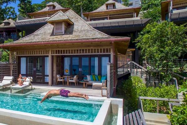 Ein Schwimmbad mit einer Person, die springt, und zwei Personen, die sich entspannen, vor dem Hilton Seychelles Northolme Resort & Spa.