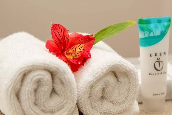Zwei weiße Handtücher mit einer roten Blume und einem kosmetischen Produkt auf einem Tisch im Occidental Eden Beruwala Hotel.
