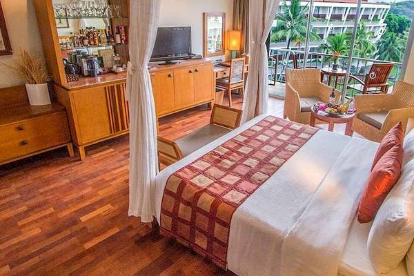 Ein elegantes Hotelzimmer im Occidental Eden Beruwala mit einem großen Bett, Holzmöbeln und einer Aussicht auf den Garten.