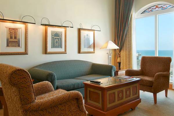 Wohnzimmer im Grand Hyatt Muscat mit Sofa, Sesseln, Tisch und Meerblick.
