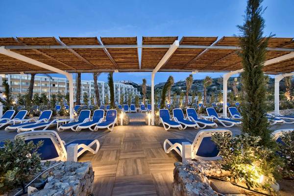 Loungebereich des db Seabank Resort & Spa bei Abenddämmerung mit blauen Sonnenliegen und Holzpavillon.