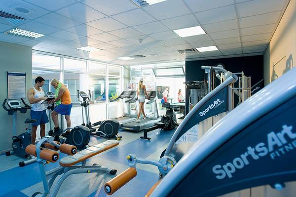 Fitnessstudio im Mediterranean Beach Hotel Zypern mit mehreren Trainingsgeräten und Personen.