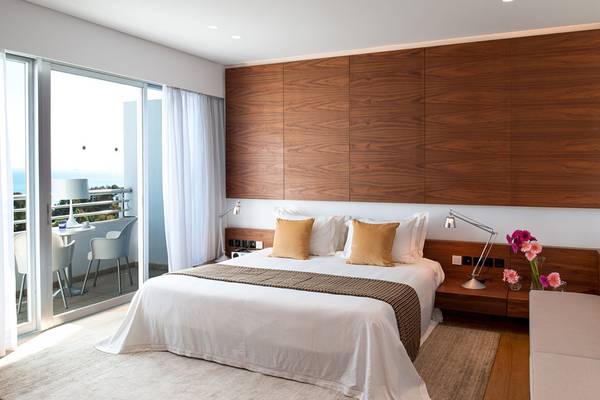 Schlafzimmer mit Balkon im Mediterranean Beach Hotel in Zypern, mit modernen Holzwänden, einem großen Bett und einem Ausblick auf das Meer.
