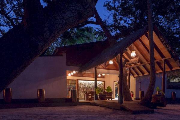 Außenansicht des Malahini Kuda Bandos Resorts bei Nacht mit beleuchtetem Eingang und umgeben von Bäumen.