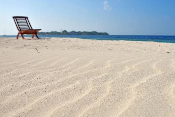 Strand mit einem Holzstuhl am Malahini Kuda Bandos Resort