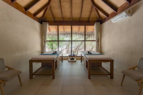 Massageraum im Malahini Kuda Bandos Resort mit zwei Betten und Blick auf Bäume.