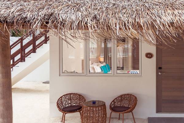 Außenansicht eines Zimmers im Malahini Kuda Bandos Resort mit zwei Korbstühlen und einem Tisch.