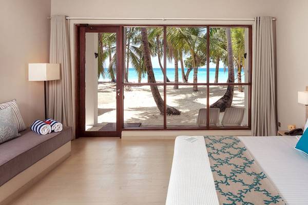 Hotelzimmer mit Panoramafenstern und Blick auf den Strand und Palmen am Malahini Kuda Bandos Resort.