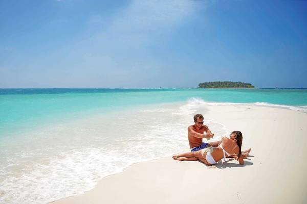 Paar am Strand von Malahini Kuda Bandos Resort mit kristallklarem Wasser und blauem Himmel