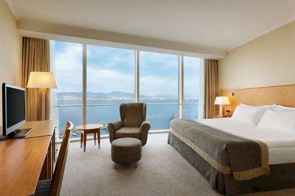 Hotelzimmer im Wyndham Grand Izmir Ozdilek mit Blick auf das Meer, Schreibtisch, Fernseher, Sessel und Bett