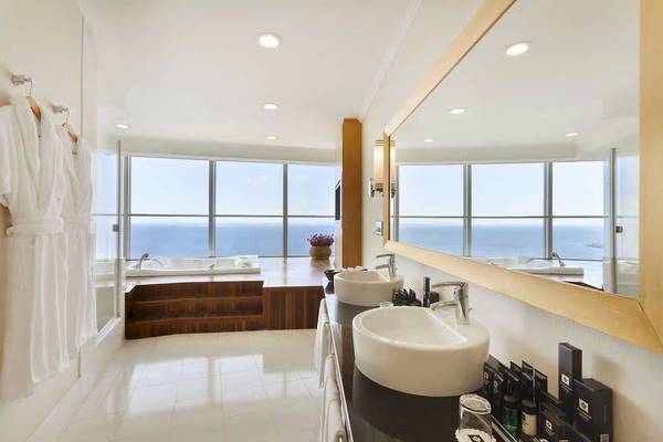 Ein modernes Badezimmer mit einem großen Spiegel, zwei Waschbecken und einem Whirlpool mit Meerblick.