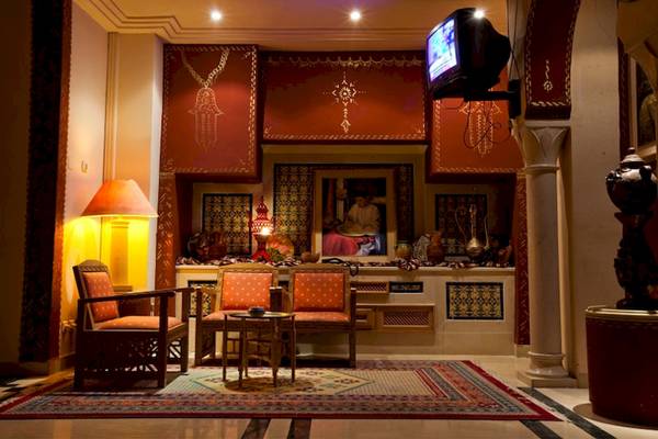 Wohnzimmer des El Mouradi Hammamet Hotels mit zwei Stühlen, einem Tisch, einem Fernseher und einem Wandbild.