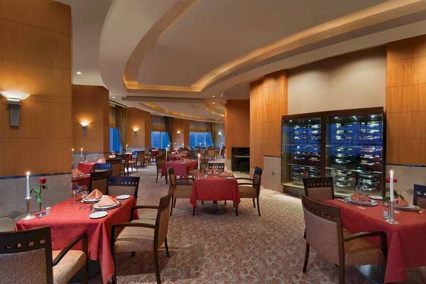 Innenansicht des Restaurants im Wyndham Grand Izmir Ozdilek Hotel mit gedämpften Lichtern und eleganten Tischen.