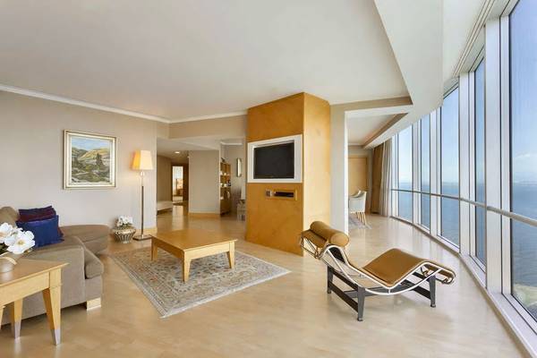 Wohnzimmer im Wyndham Grand Izmir Ozdilek mit Meerblick, Couch, Teppich, Tisch und Fernseher.
