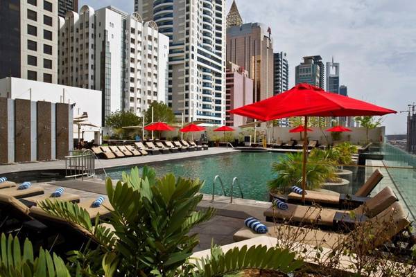 Poolbereich des Tower Plaza Hotel Dubai mit roten Sonnenschirmen und Liegestühlen.