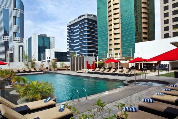 Außenpoolbereich des Tower Plaza Hotel Dubai mit Loungeliegen und roten Sonnenschirmen.